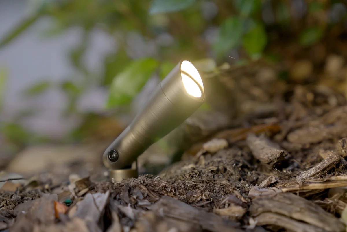 Brass landscape uplight beside plants in a mulched garden bed
