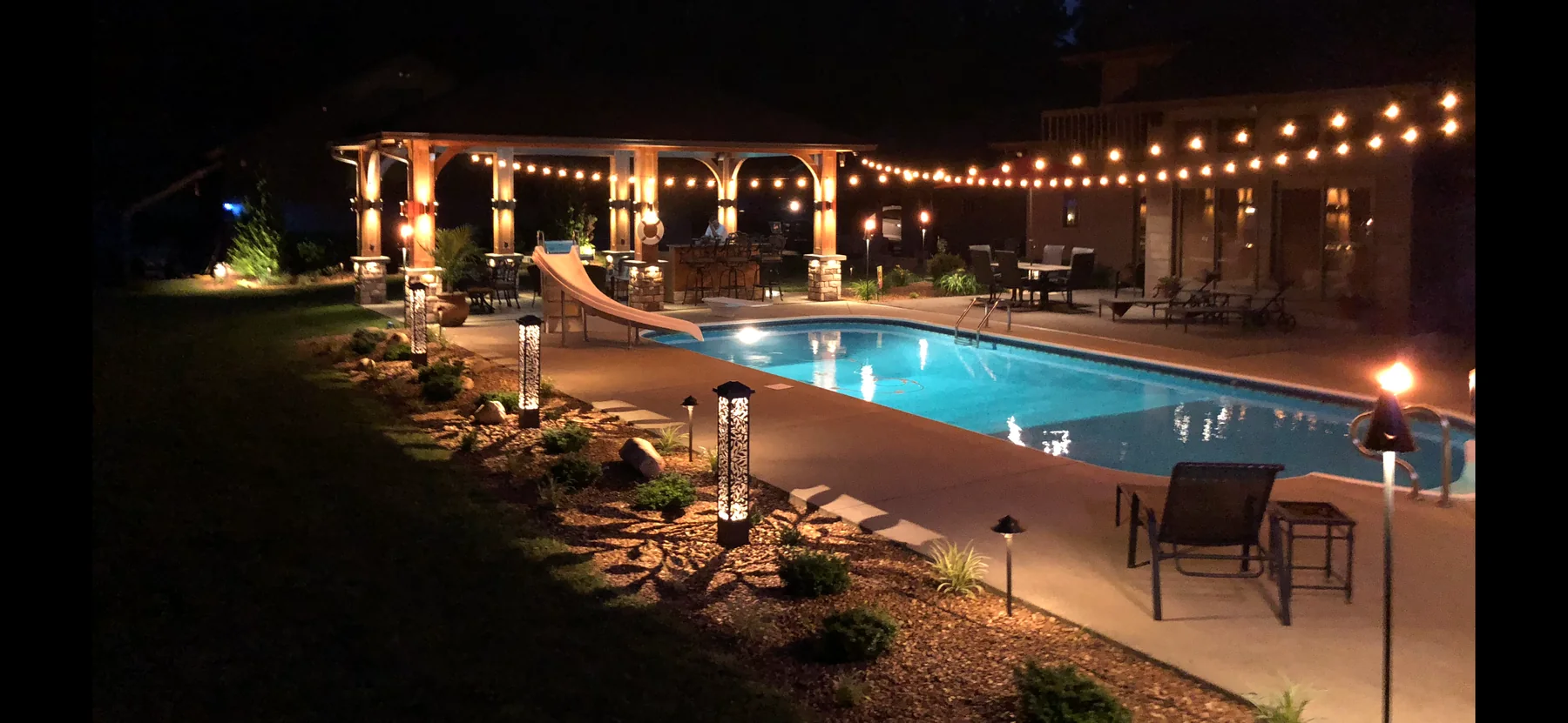 Pool and patio with string lights and warm landscape lighting at night