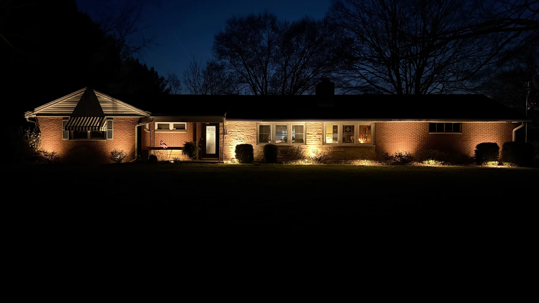 Warm uplighting across a single-story home and front landscape at night