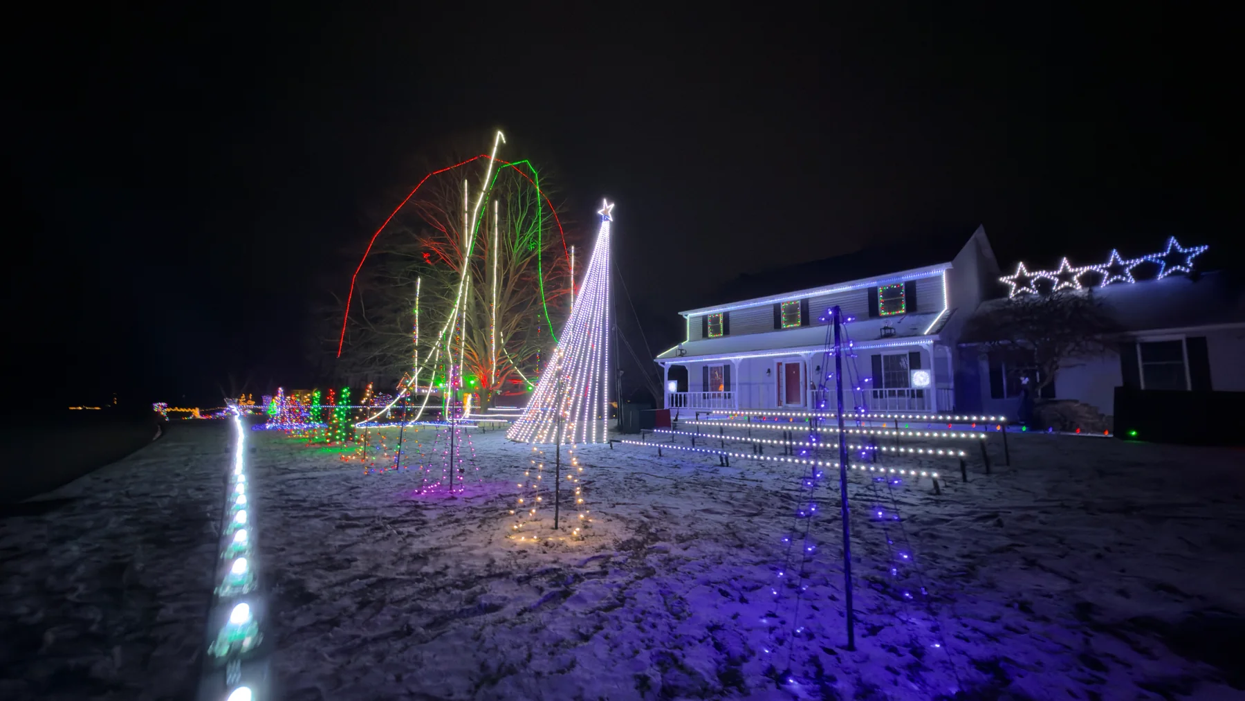 Seasonal Christmas lights outlining a snow-covered home and garden tree
