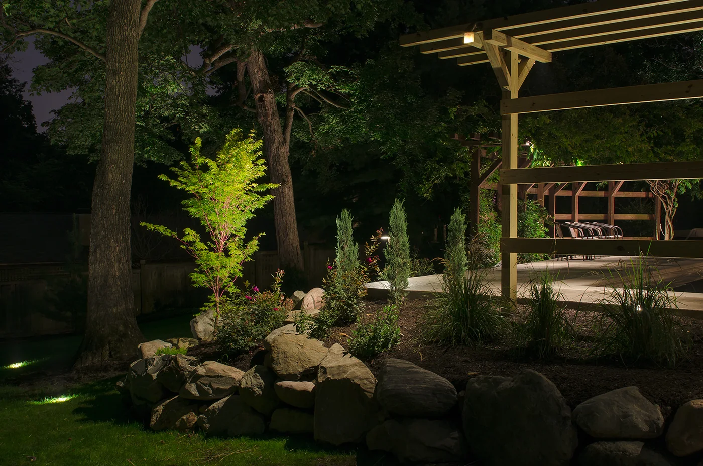 Warm lighting on a garden tree, stone planting bed and pergola