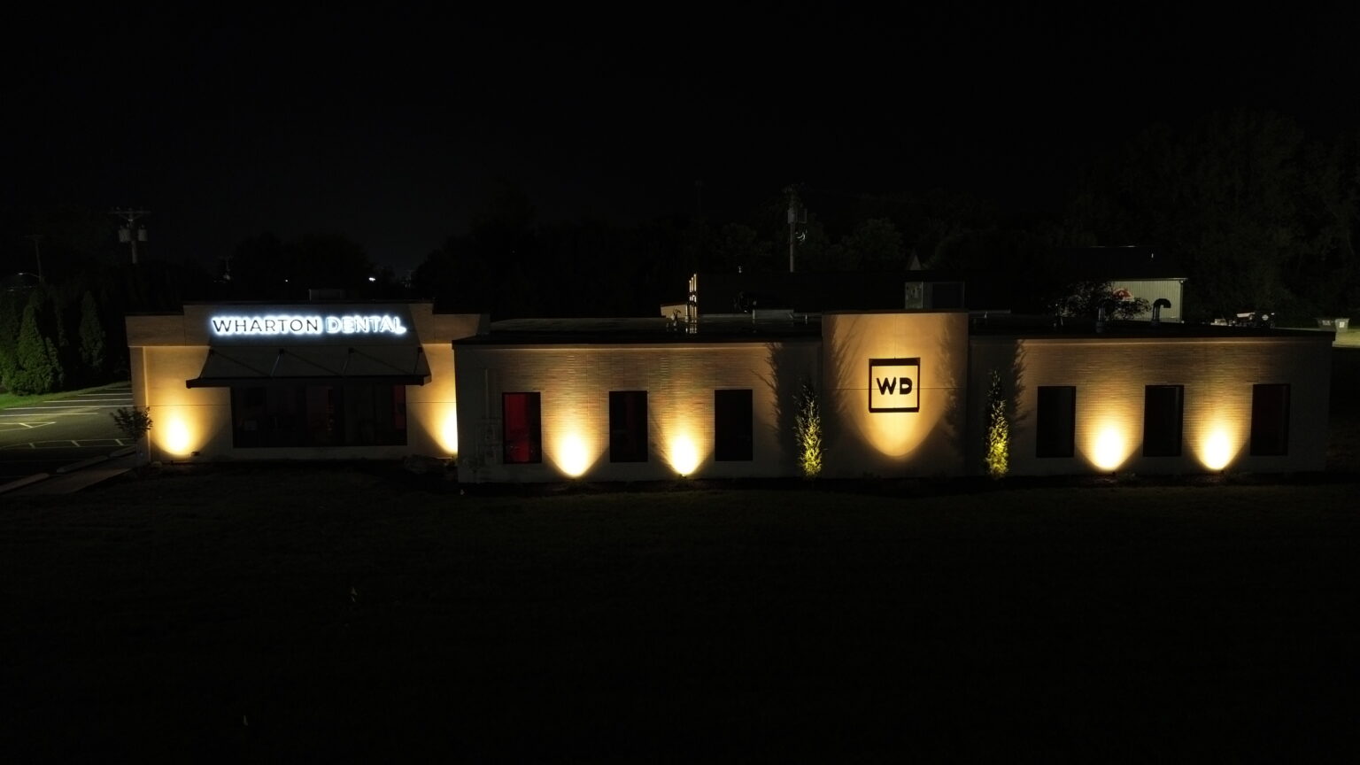 Warm architectural uplighting across the Wharton Dental facade